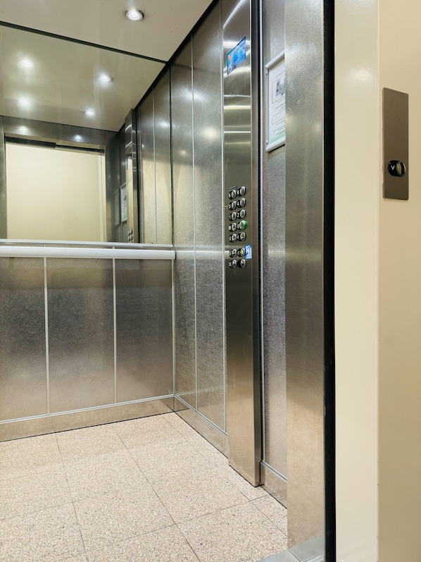 An elevator with a control panel, metallic walls, and a tiled floor.