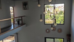 Un interior con varios niveles, un balcón, lámparas colgantes y vistas a través de una ventana.