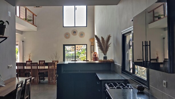 Una cocina moderna con una isla central, un comedor con sillas de madera y un amplio ventanal que ofrece vistas al exterior.