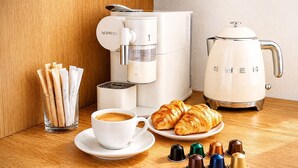 Une machine à café, une tasse de café, des croissants et des dosettes de café sur une table en bois.