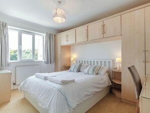 Ein Schlafzimmer mit Bett, Fenster, Vorhängen, Heizkörper, Nachttisch mit Lampe und Holzschränken.