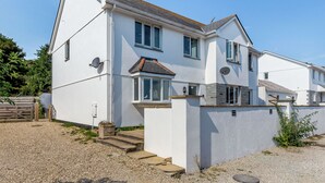 A two-story house with a white exterior, a small front porch, and a gravel driveway. - 8 Harlyn Mews (Padstow)