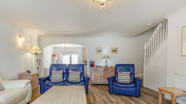 A living room with a sofa, chairs, a coffee table, a staircase, and a hallway leading to a kitchen. - 8 Harlyn Mews (Padstow)