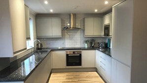 A modern kitchen with a dishwasher, oven, and stainless steel appliances. - 8 Harlyn Mews (Padstow)