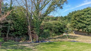 A grassy backyard with trees, a swing set, and a fence. - 8 Harlyn Mews (Padstow)