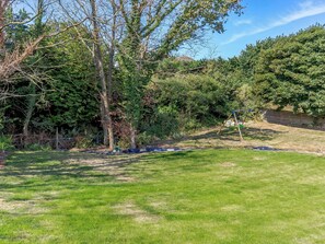 A grassy backyard with trees, a swing set, and a fence. - 8 Harlyn Mews (Padstow)