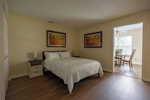 A bedroom with a bed, nightstands, a dresser, two framed paintings, and a dining area with a table and chairs. - Keystone Garden Villa C (Indianapolis)