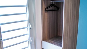 Una stanza con un'armadio in legno, una porta bianca e una finestra con persiane orizzontali.