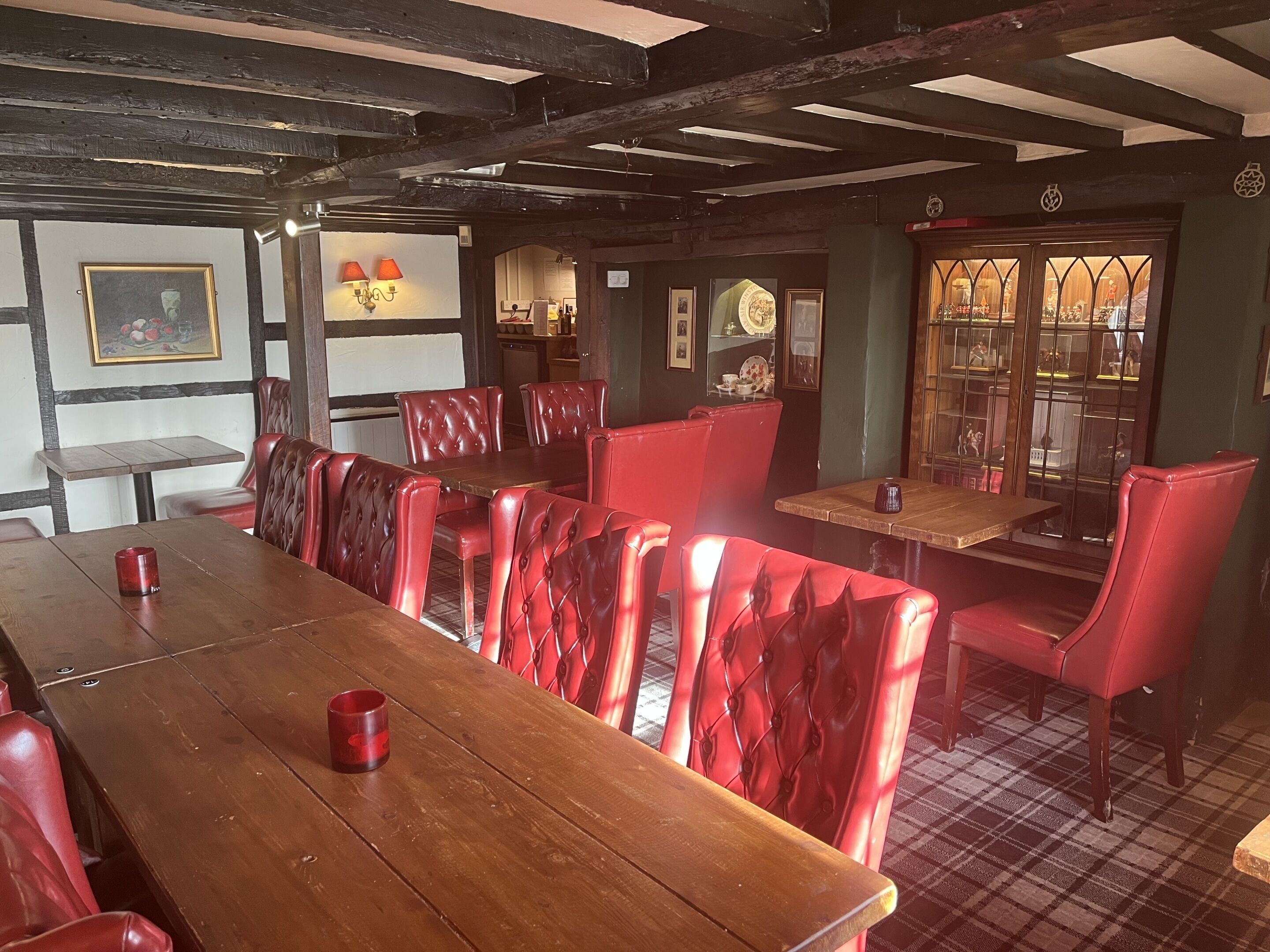 A restaurant with wooden tables and red upholstered chairs, a high ceiling with exposed beams, and a checkered floor.