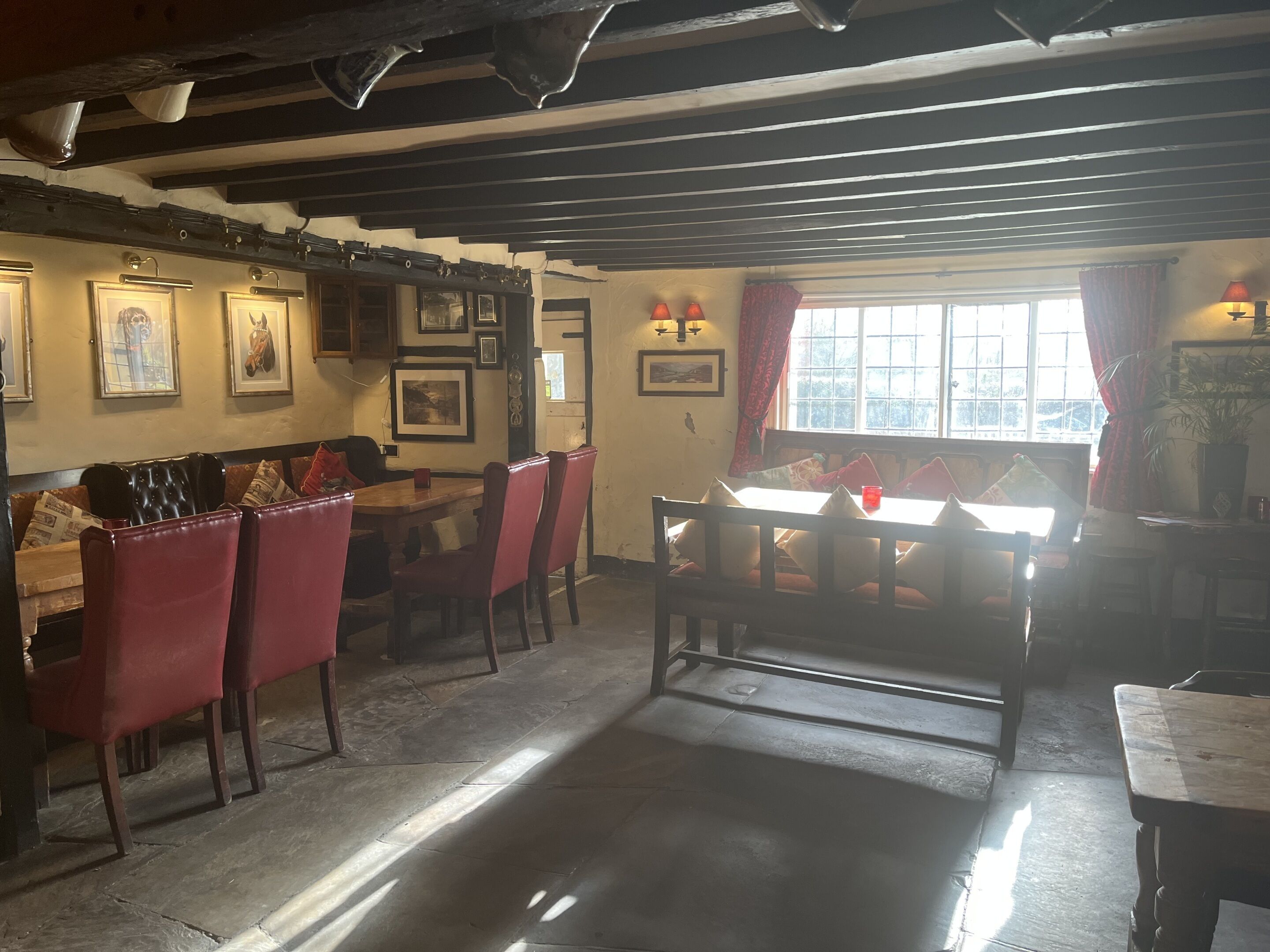 Un comedor con mesas y sillas de madera, cuadros en las paredes y una ventana con cortinas.