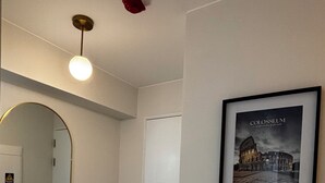 En hall med en rund spegel, en inramad tavla som föreställer Colosseum, en vit dörr och en lampa i taket.