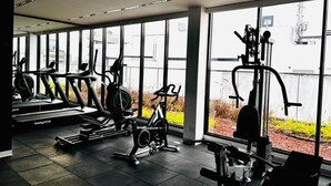 Ett gym med löpband, motionscyklar och styrketräningsmaskiner, stora fönster och utsikt över omgivningarna.