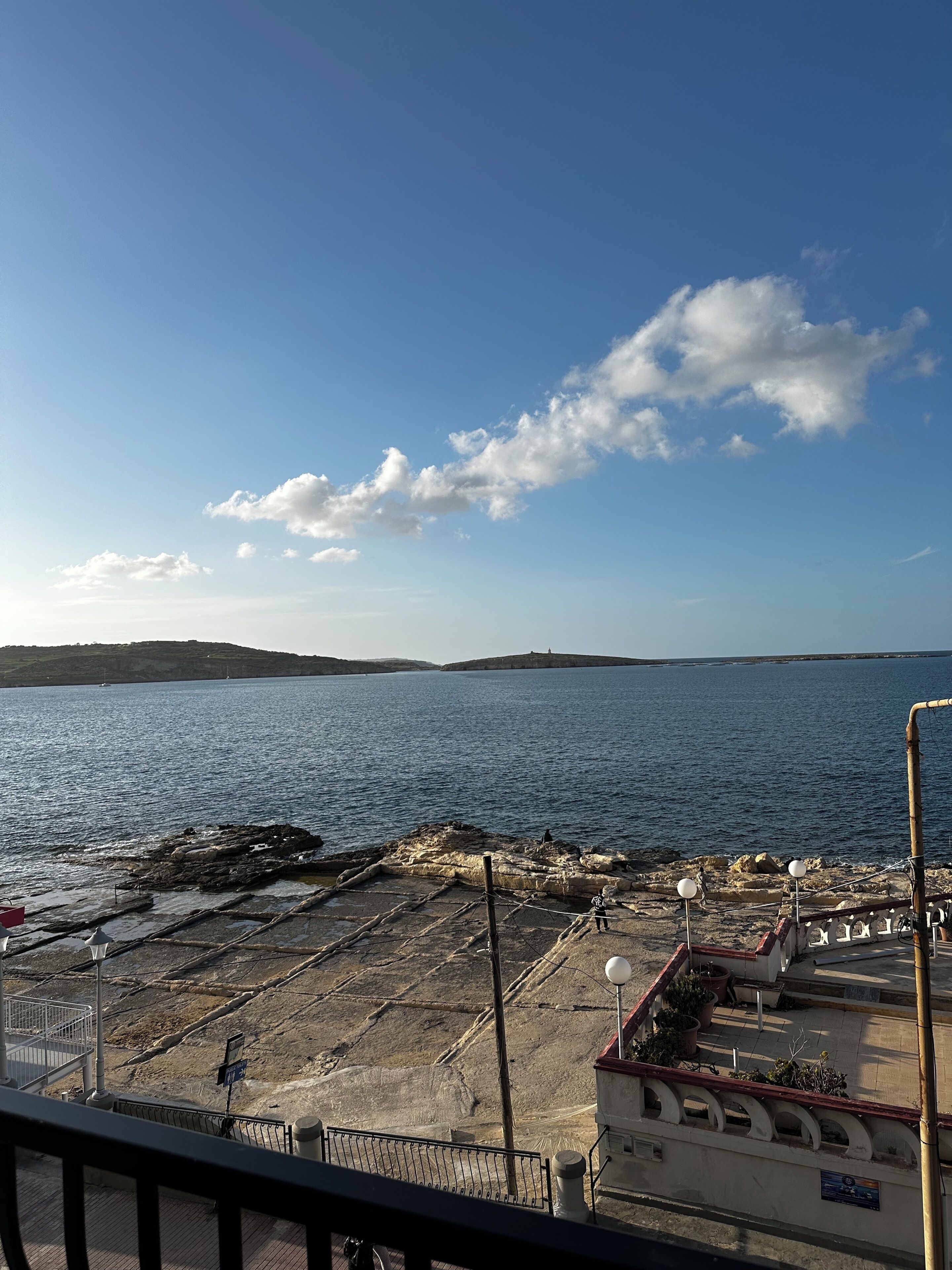 A coastal view with a rocky shoreline, a clear sky, and a distant landmass.