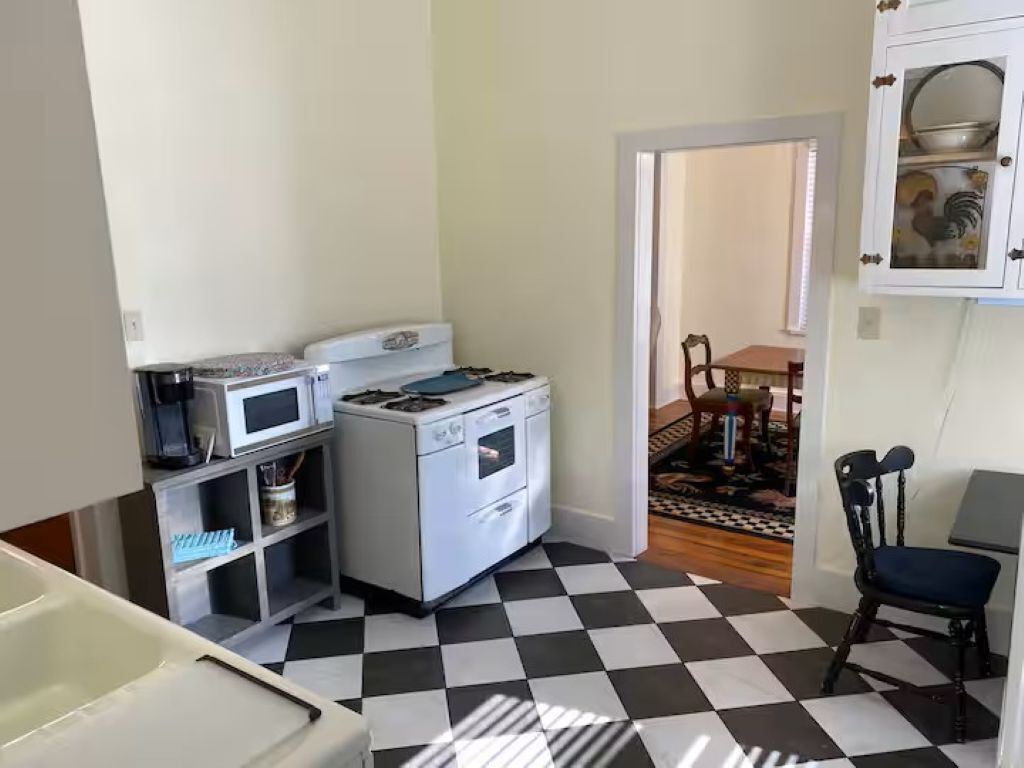 Une cuisine compacte équipée d’un four à micro-ondes, d’une cuisinière et d’un évier, un coin repas avec une table et des chaises, et un sol à carreaux.