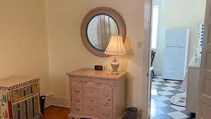 A bedroom with a bed, dresser, mirror, lamp, and a view of a hallway with a checkered floor. - Historic Bisbee Retreat - Huge Private Porch -Walk to Town (Bisbee)