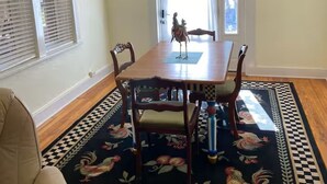 A dining area with a wooden table, four chairs, a chandelier, a patterned rug, and a window with blinds. - Historic Bisbee Retreat - Huge Private Porch -Walk to Town (Bisbee)