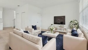 En moderne stue med en sofa, et sofabord og et fjernsyn monteret på væggen.
