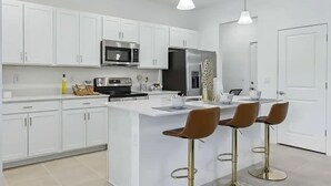 Une cuisine moderne avec des meubles blancs, des appareils en acier inoxydable et un îlot central doté de tabourets de bar.