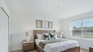 Une chambre à coucher avec un lit en bois, deux tables de chevet, une fenêtre avec des stores et une porte.