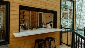 Une cabane en bois comprenant un coin cuisine, un balcon avec une balustrade et une grande fenêtre.