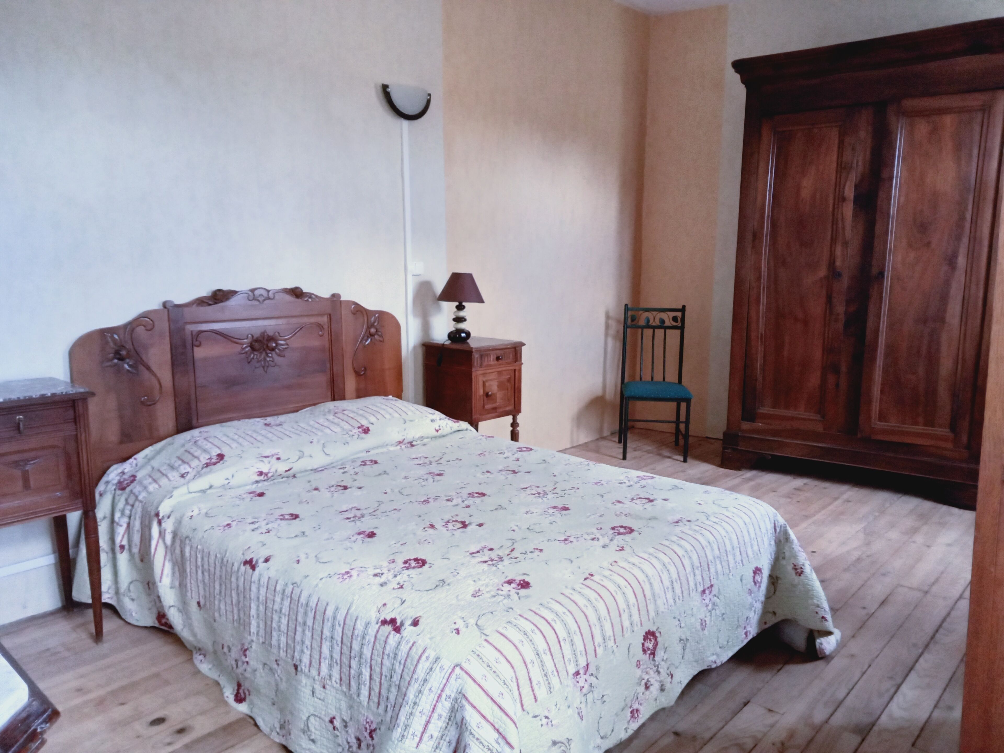 Un dormitorio con una cama de madera, una mesita de noche, una silla y un armario.