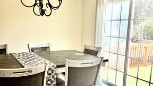 Un espace repas comprenant une table, des chaises, un lustre et une porte-fenêtre coulissante donnant sur une terrasse.