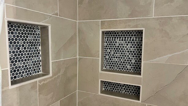 Un mur recouvert de carreaux, avec trois niches carrées contenant des motifs circulaires.