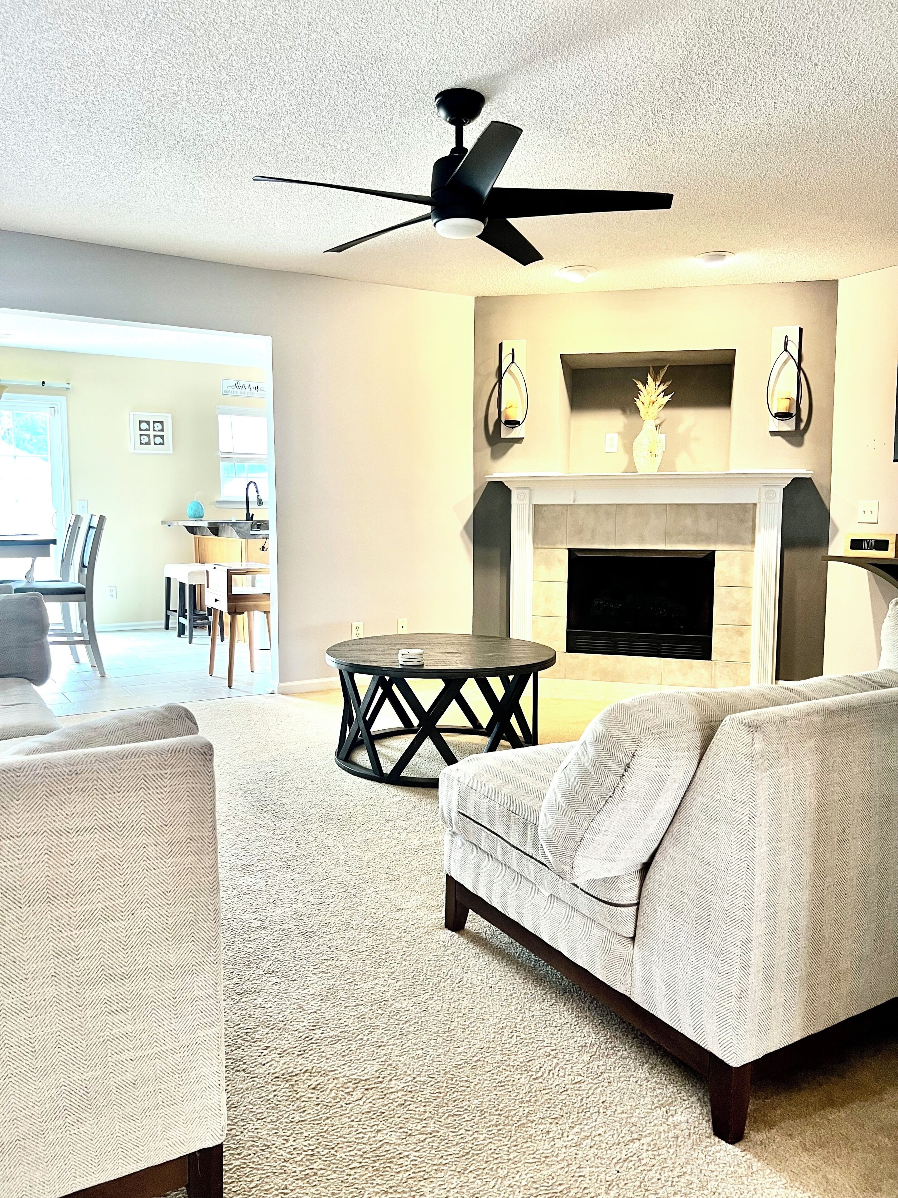 A living room with a fireplace, a ceiling fan, and a dining area visible in the background.