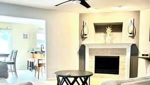 Un salon doté d’une cheminée, d’un ventilateur de plafond et d’un coin repas visible au fond.