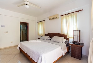 Ein Schlafzimmer mit Bett, Nachttisch, Spiegel, Deckenventilator und Klimaanlage.