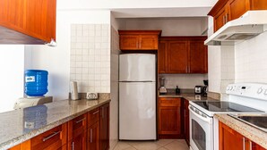 Una cocina con armarios de madera, un refrigerador blanco, una estufa y un dispensador de agua azul.