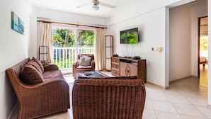 Una habitación con mobiliario de mimbre, ventilador de techo, televisión y balcón con cortinas.