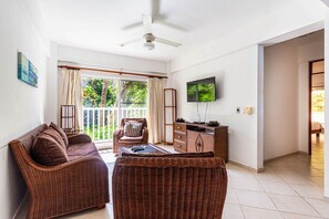 Ein Zimmer mit Korbmöbeln, einem Deckenventilator, einem Fernseher und einem Balkon mit Vorhängen.