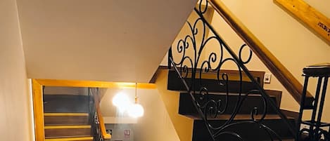 A wooden staircase with a black metal railing, a mirror on the wall, and a light fixture above the stairs.