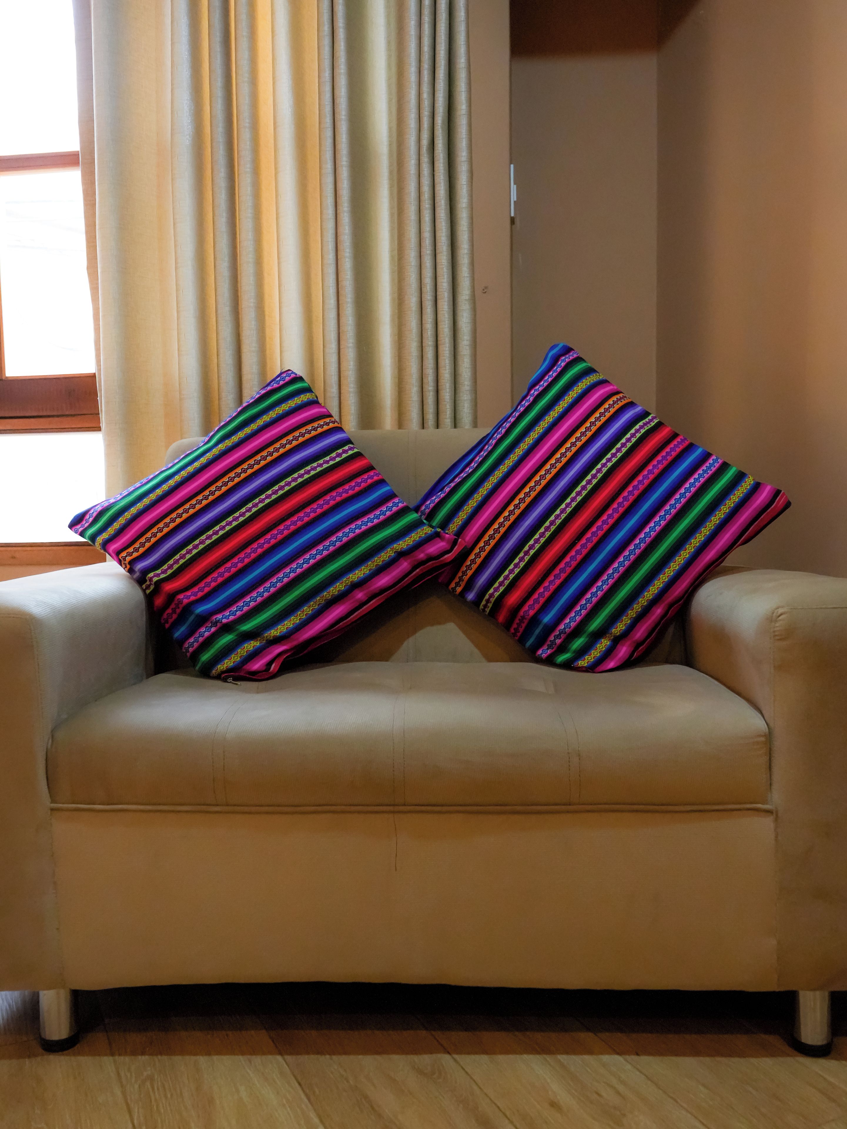 A beige sofa with two colorful striped pillows.