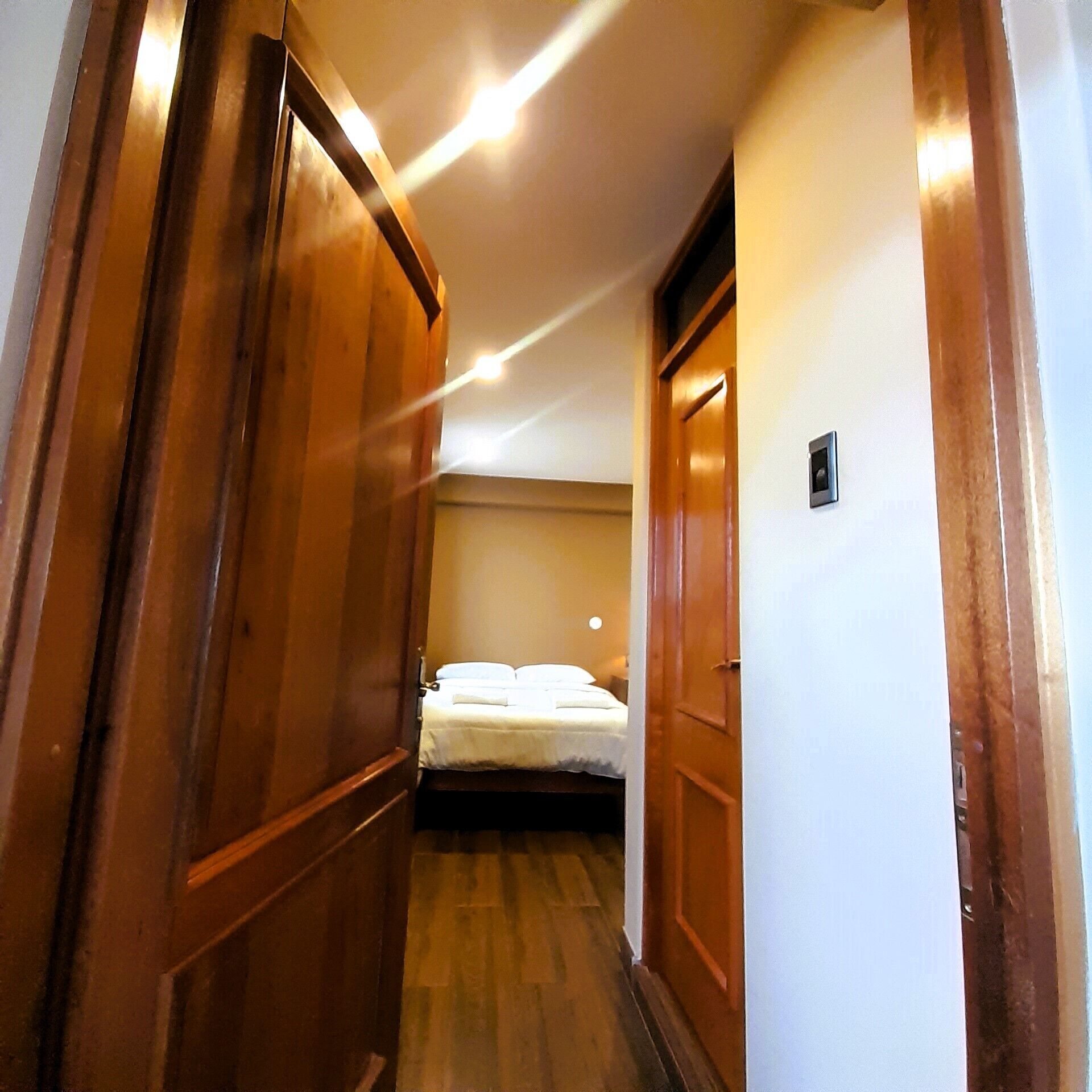 A narrow hallway leading to a bedroom with a bed and a nightstand.