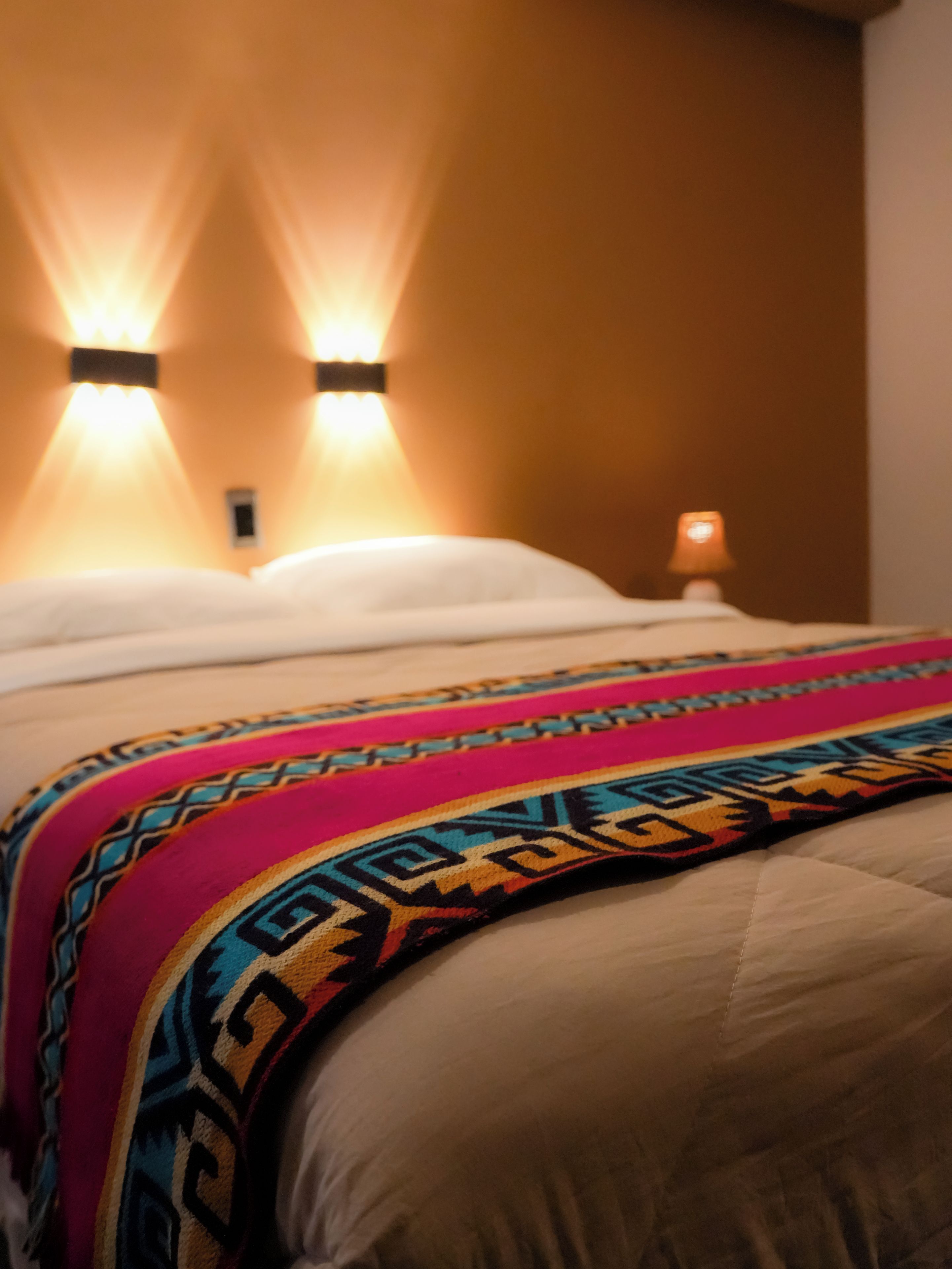 Una cama con un edredón estampado y dos luces fijadas a la pared.