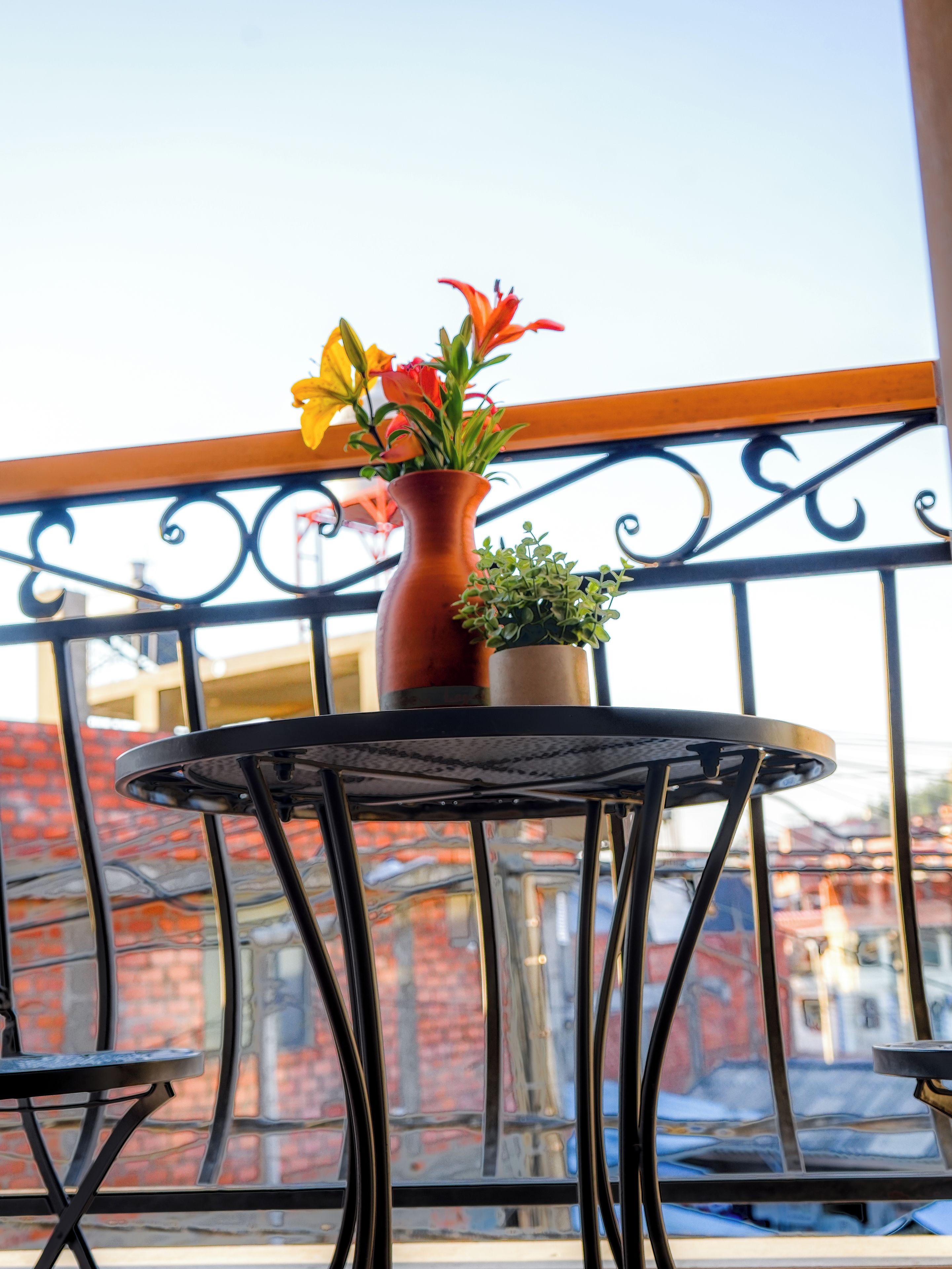 Een ronde tafel met een bloevas en een kleine plant op een balkonhek.