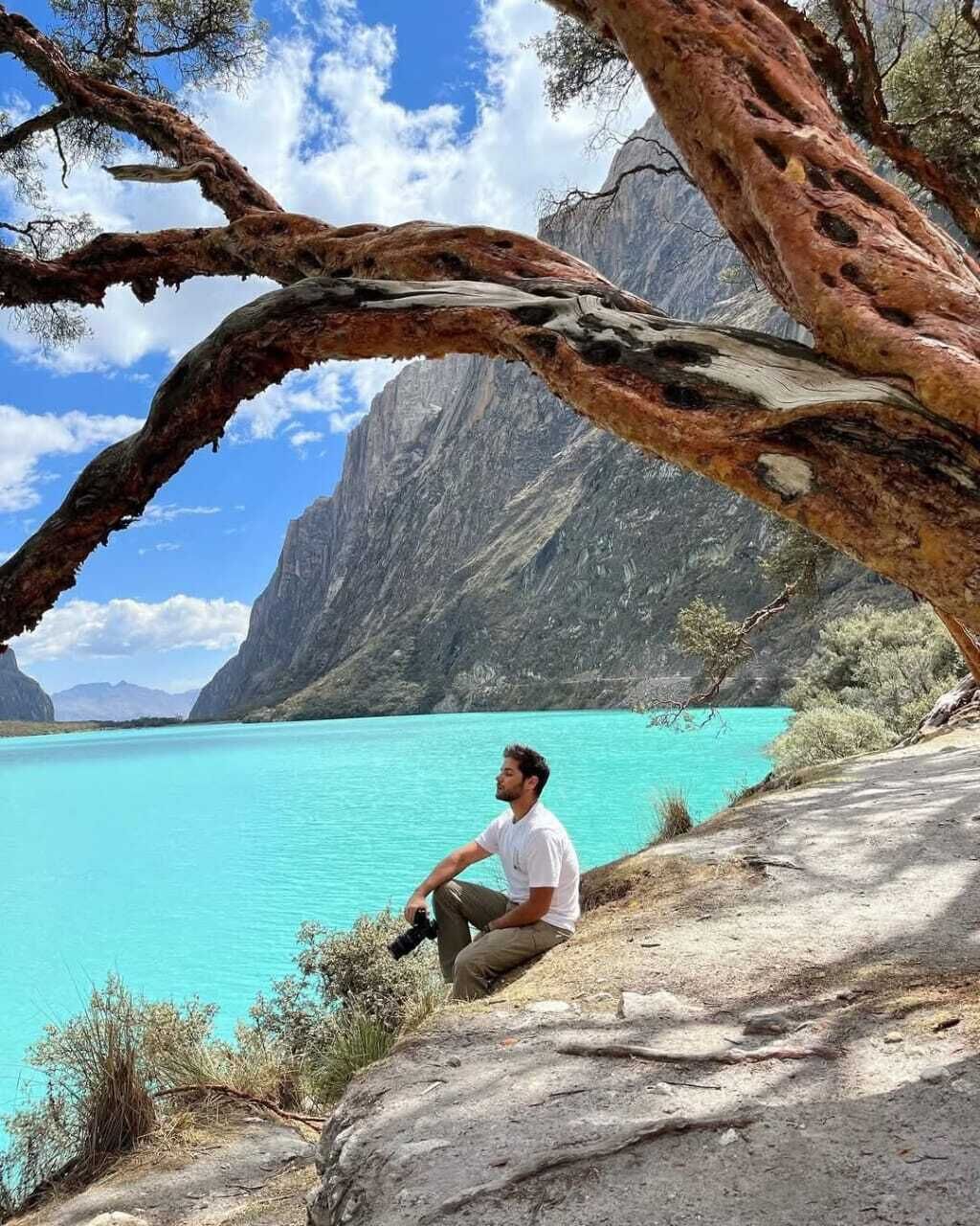 A person sitting on a rocky ledge overlooking a turquoise lake with mountains in the background.