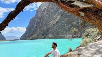 A person sitting on a rocky ledge overlooking a turquoise lake with mountains in the background.