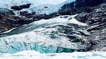 A person seated on a snow-covered ledge overlooking a glacier with turquoise water.