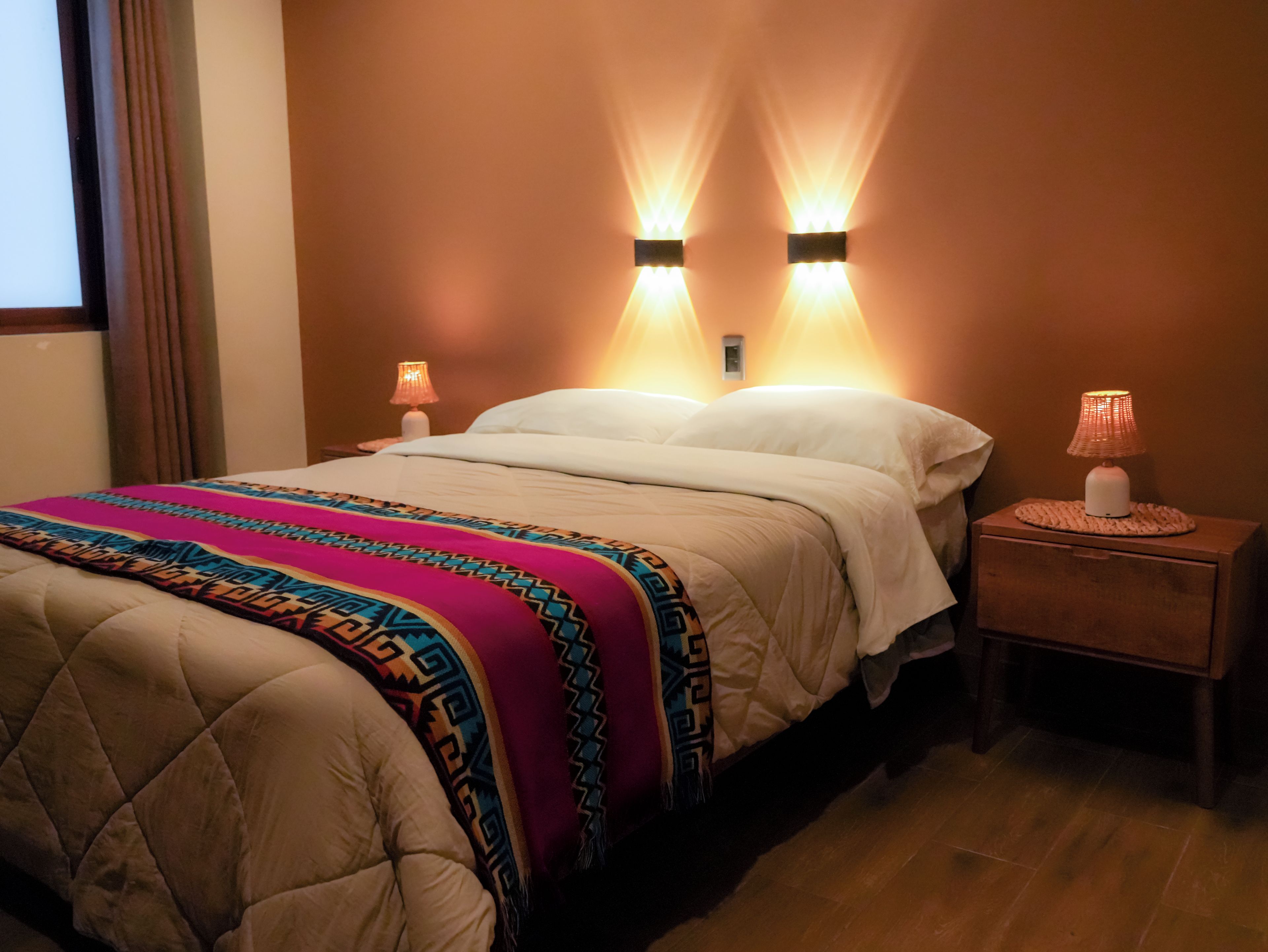 Una habitación de hotel con una cama, dos lámparas de noche y una mesita de noche.
