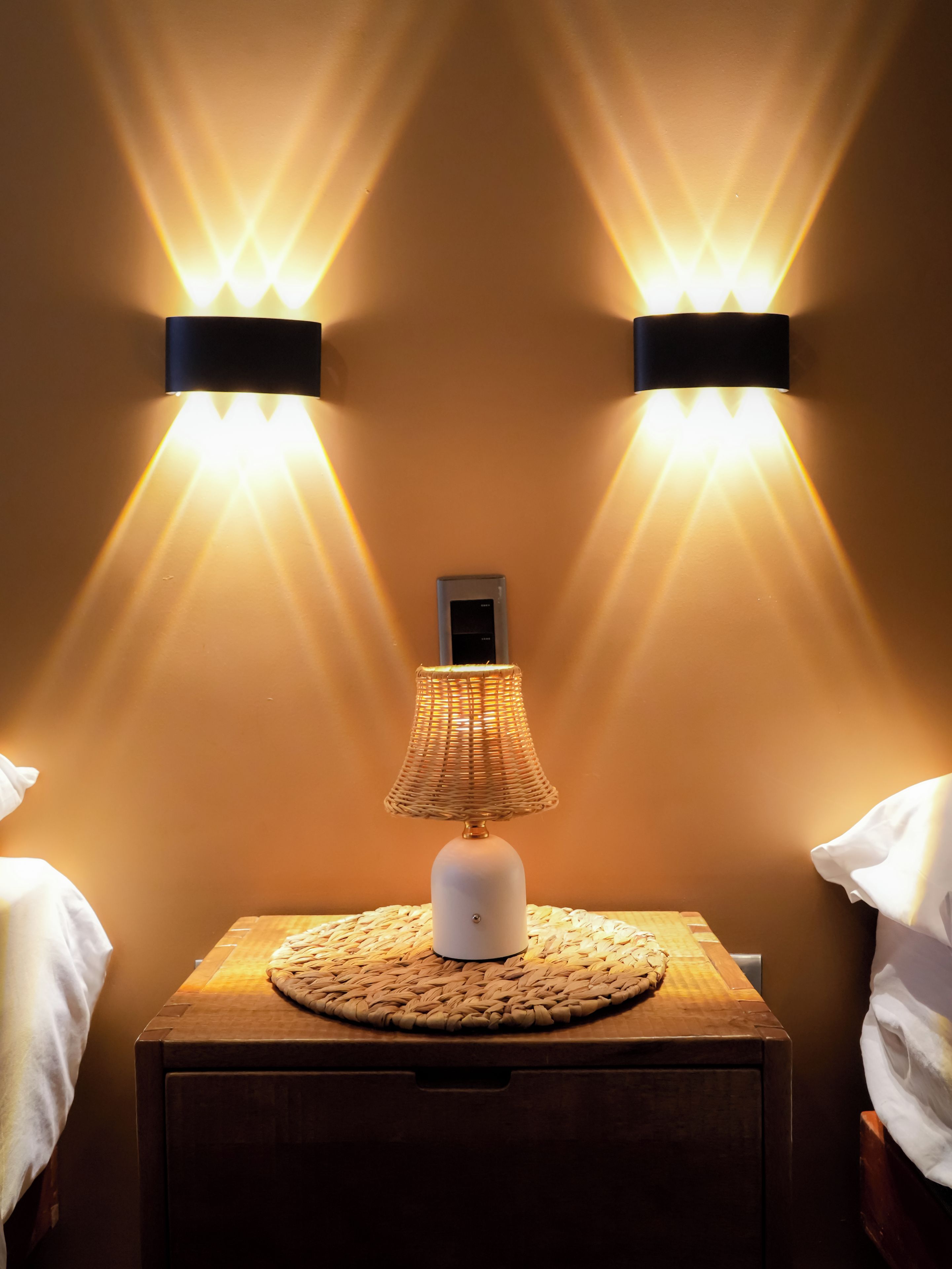 A nightstand with a lamp and two wall-mounted lights.