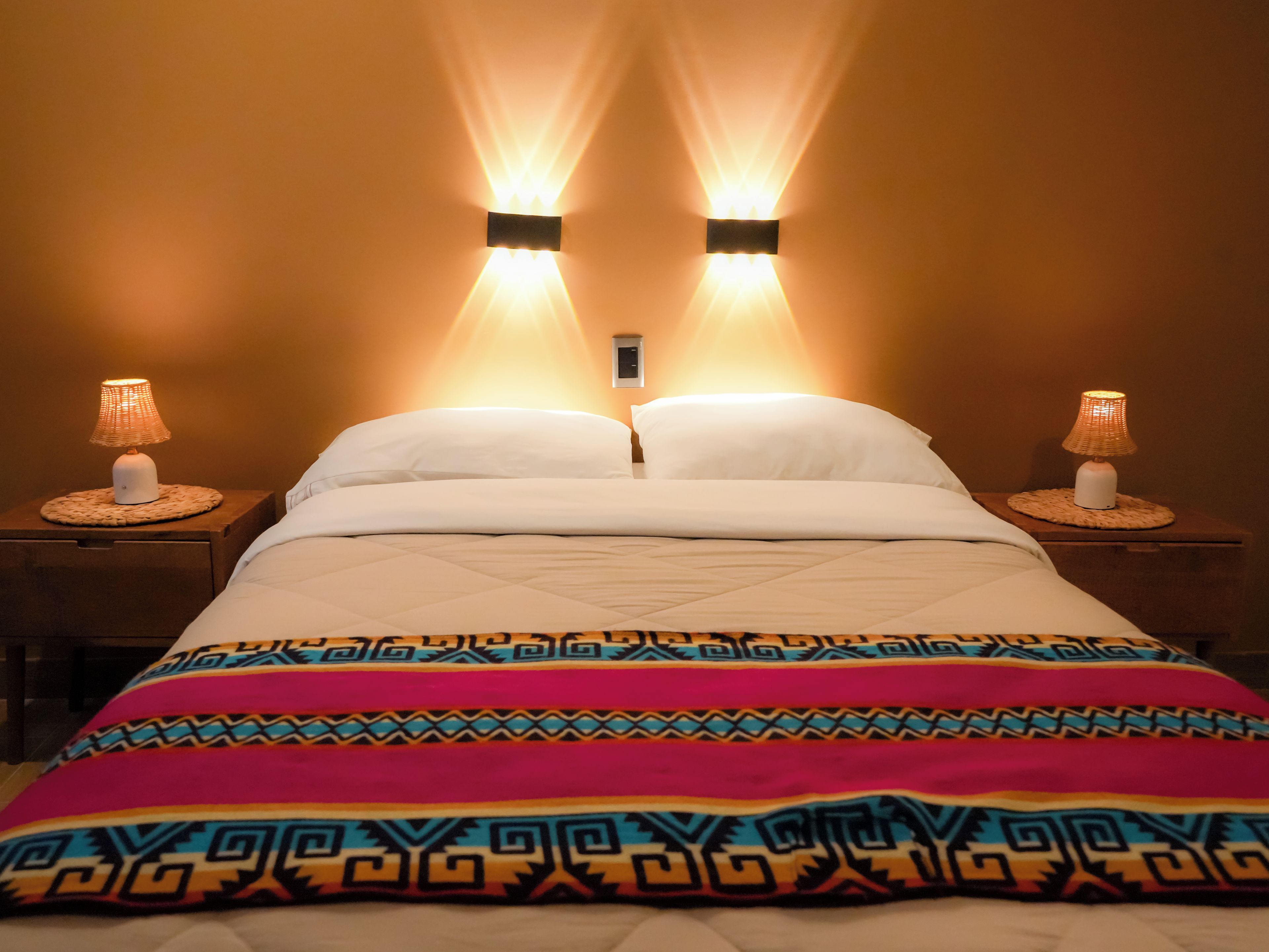 Ein Bett mit einer gemusterten Decke, zwei Nachttischlampen und einer Wandleuchte.