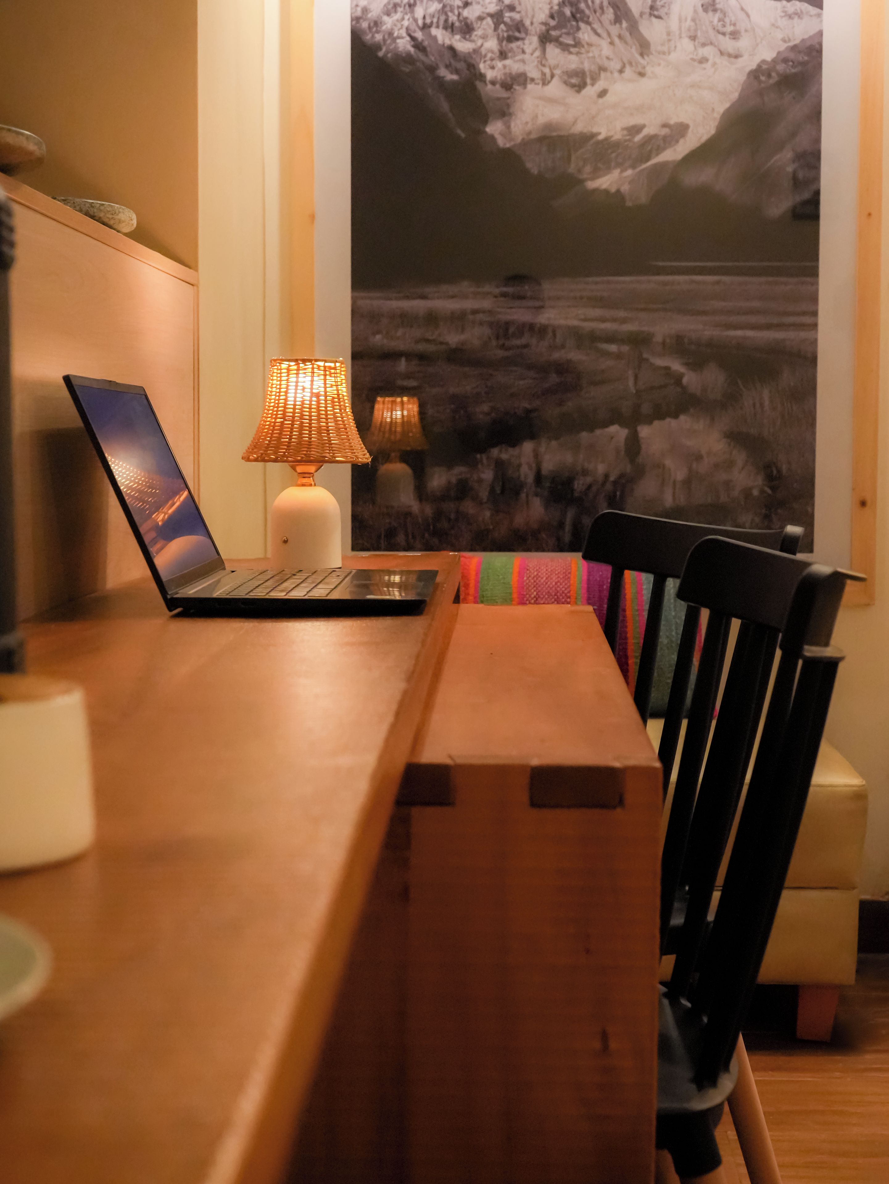A wooden desk with a laptop, two lamps, and a colorful chair.