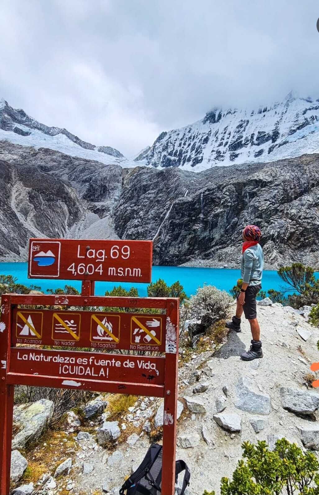 Señal de sendero de montaña con vista a un lago, un excursionista y una mochila.