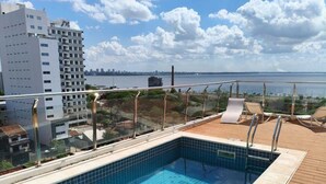 Una piscina en la azotea con vistas al horizonte de la ciudad y una masa de agua a lo lejos.