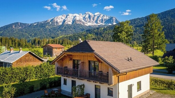 Un chalet doté d’un balcon, entouré de verdure et avec une vue sur les montagnes.