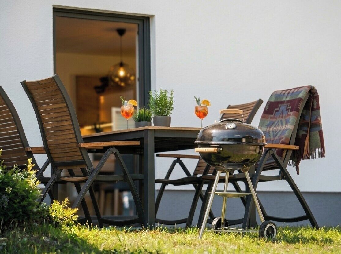 Een eethoek buiten met een tafel, stoelen, een barbecue en twee drankjes.