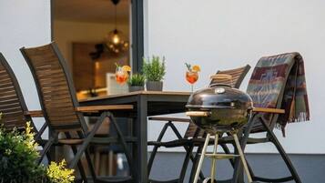 Een eethoek buiten met een tafel, stoelen, een barbecue en twee drankjes.